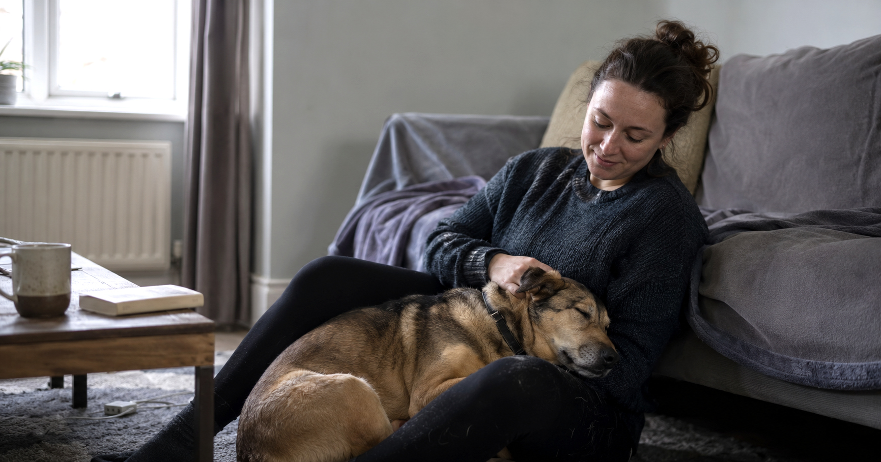 A woman sitting on the floor of a UK living room with her emotional support dog resting its head in her lap